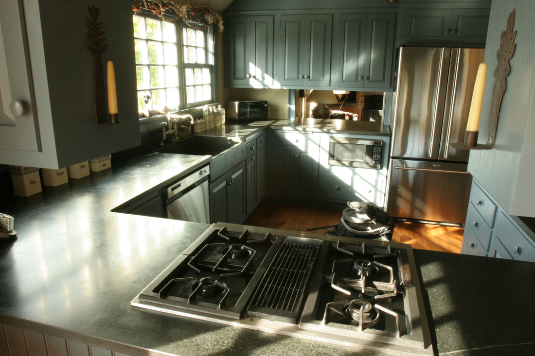 A green, gray counter NEHS installed in a kitchen. Sun is shining over the counter, sink, and cabinets.